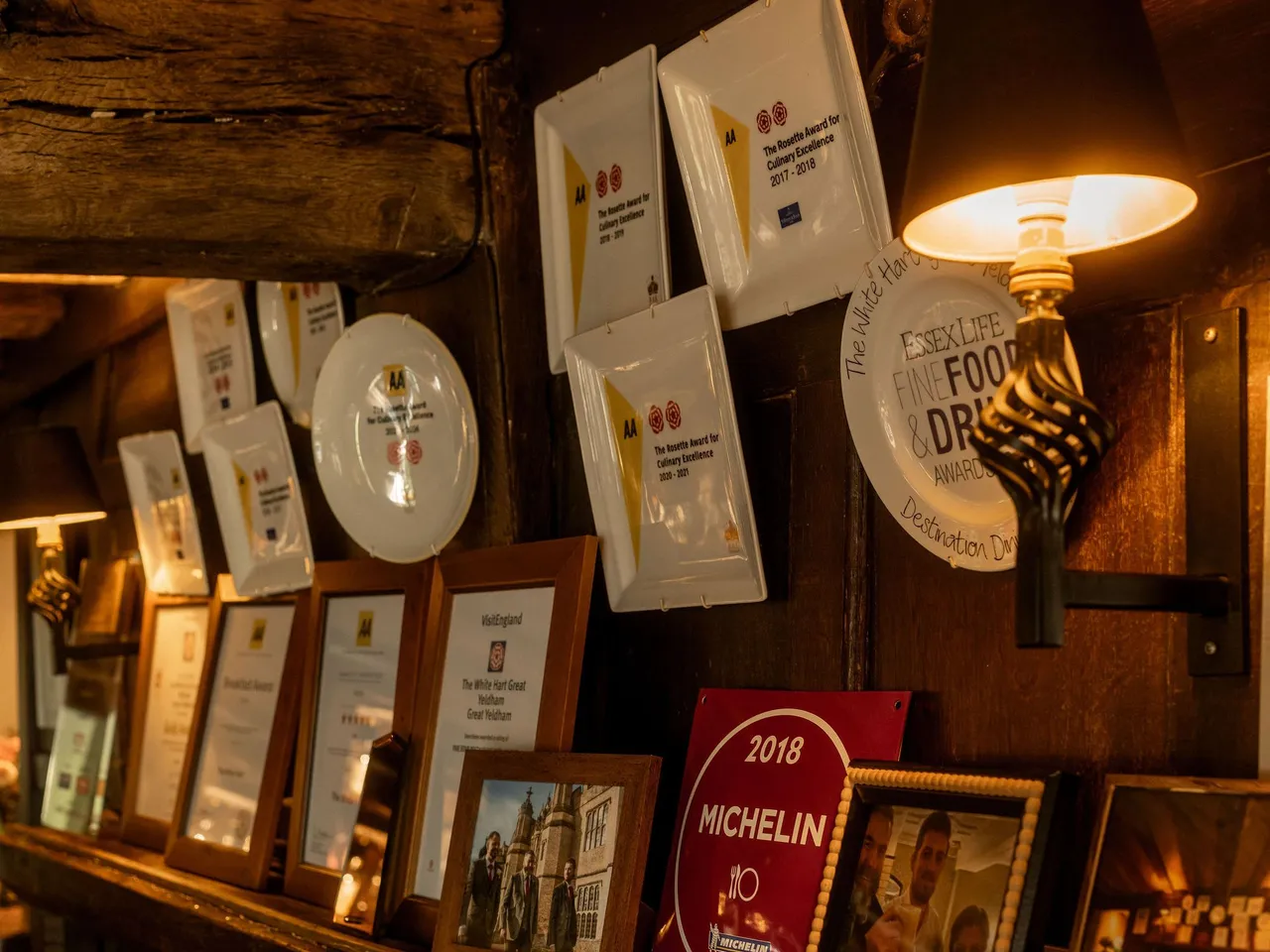 A rustic wooden shelf adorned with framed awards, certificates, a Michelin plaque, and photographs inside a cozy restaurant.