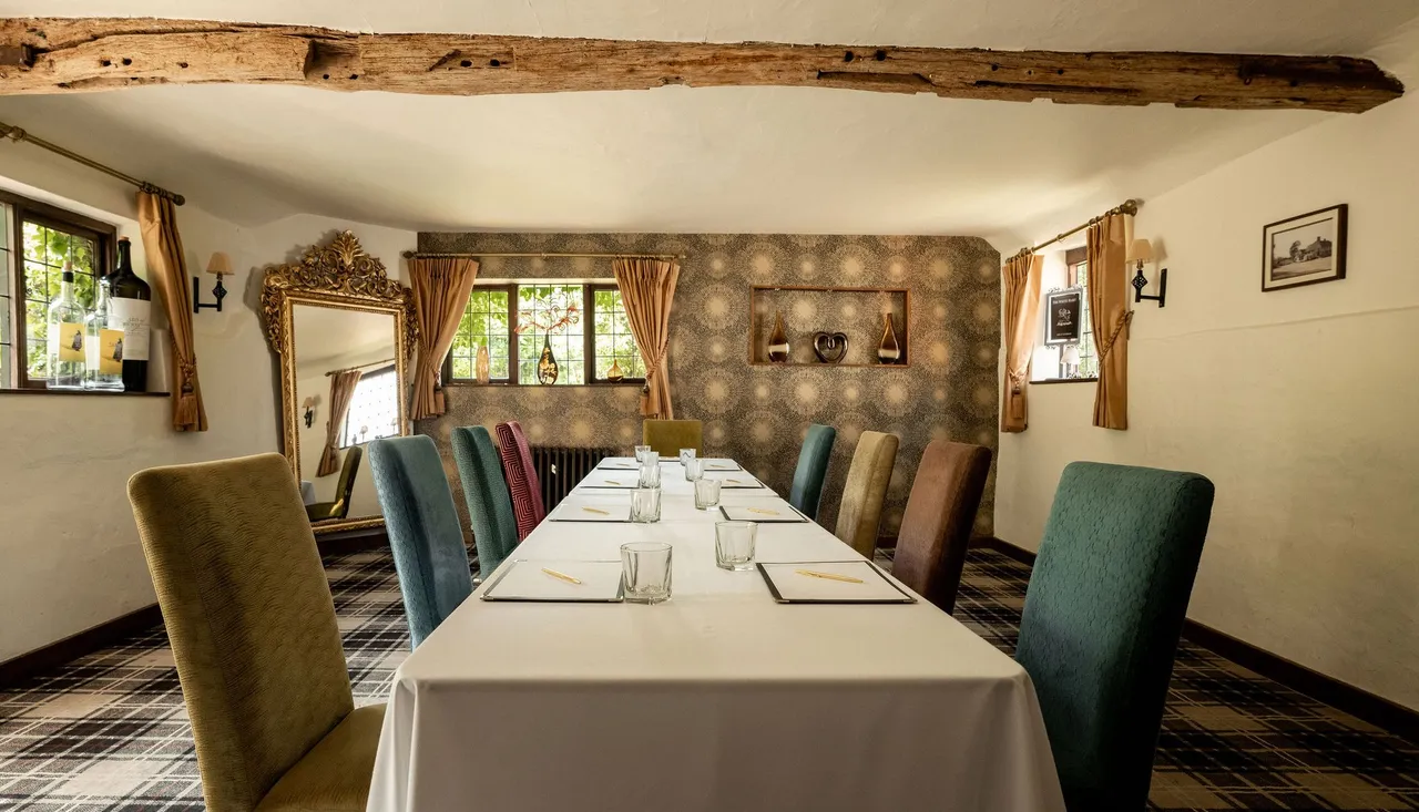 A cozy meeting or dining room with a long table, assorted colorful chairs, and rustic decor.