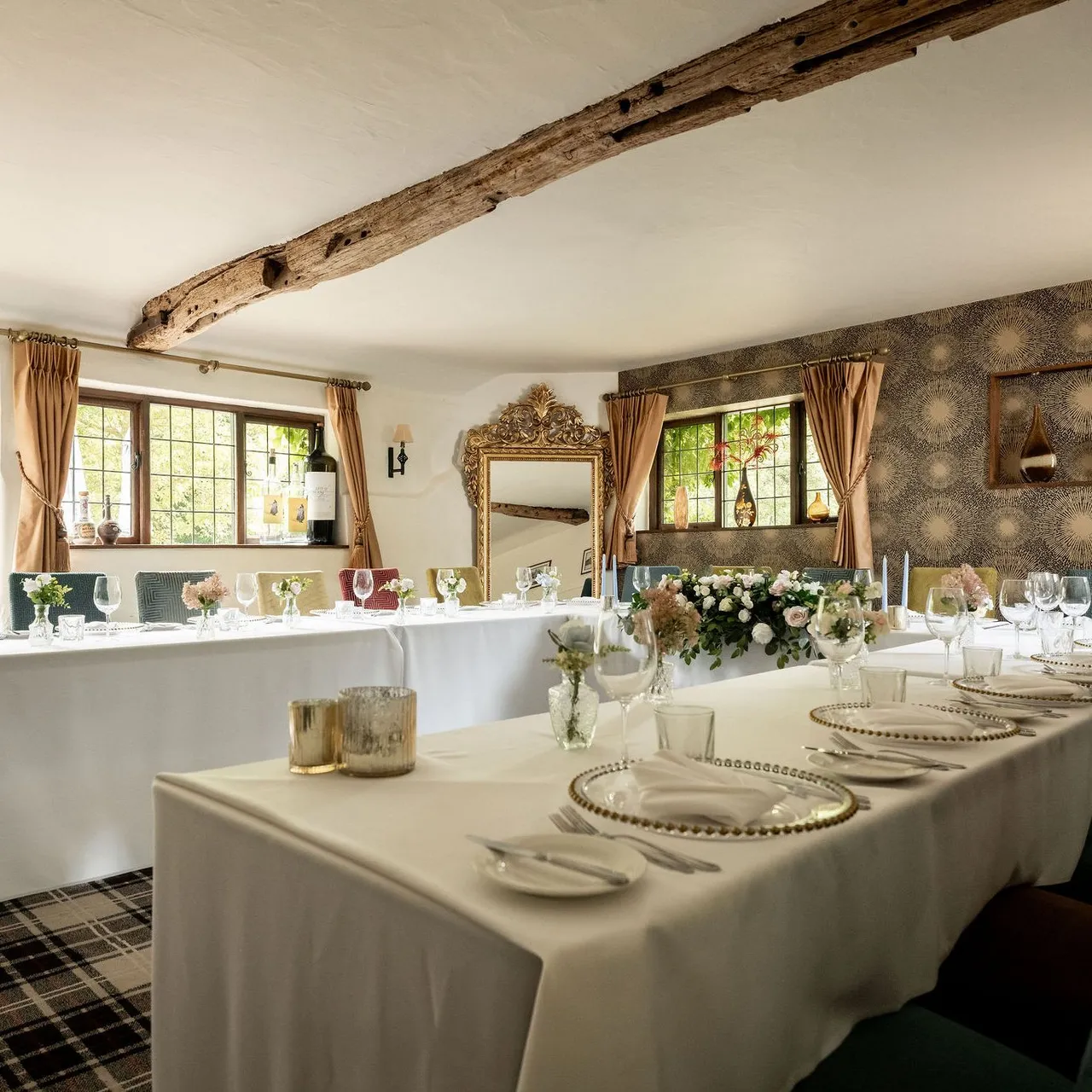 Elegant dining room setup with white tablecloths, floral centerpieces, and decorative elements in a cozy, light-filled space.