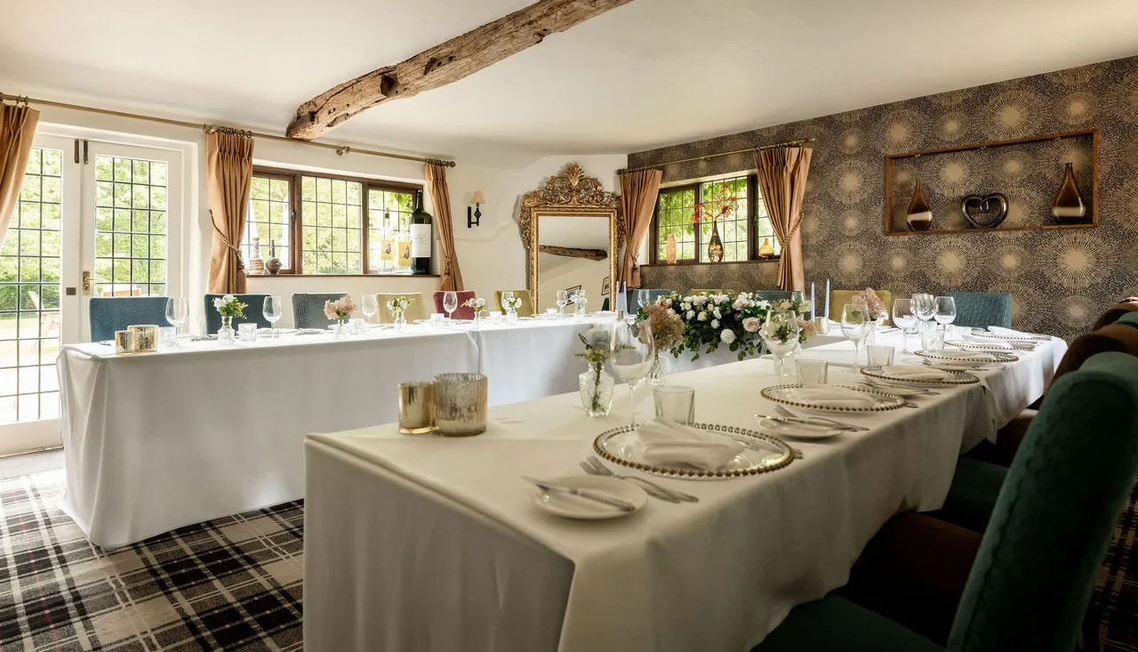 Elegant dining room setup with white tablecloths, floral centerpieces, and decorative elements in a cozy, light-filled space.