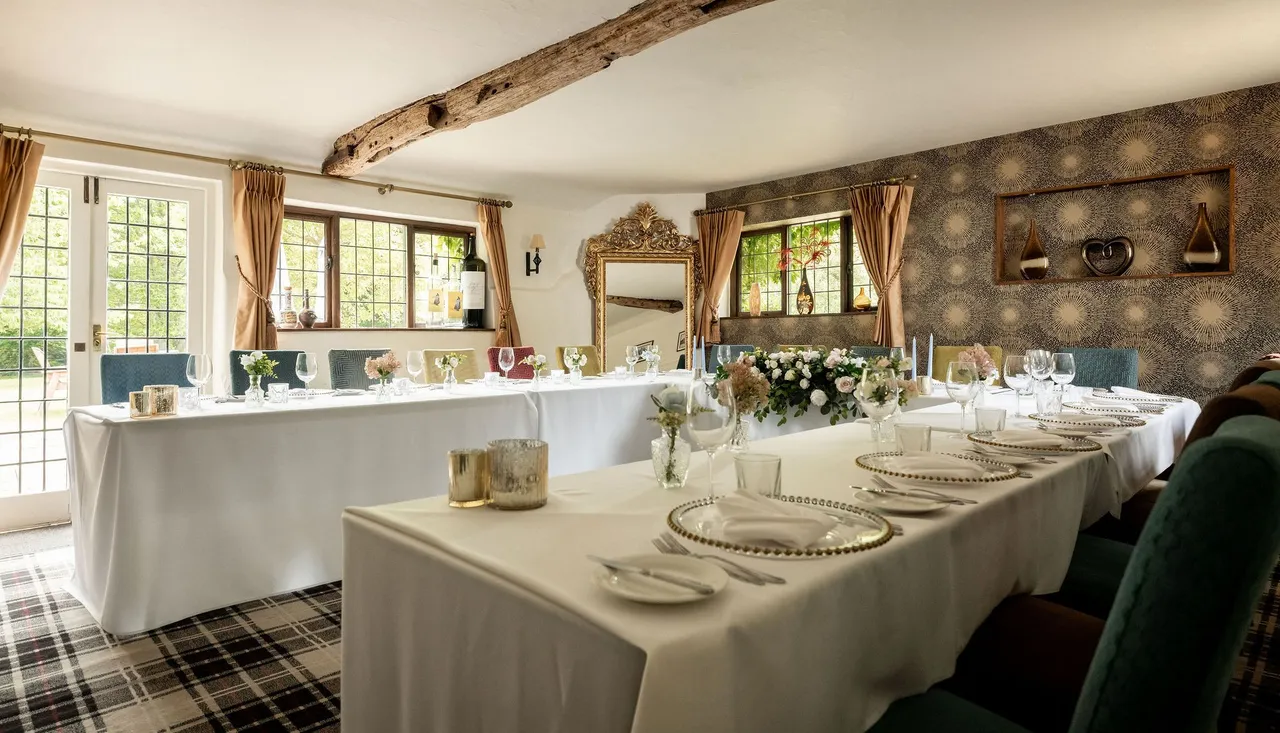 Elegant dining room setup with white tablecloths, floral centerpieces, and decorative elements in a cozy, light-filled space.