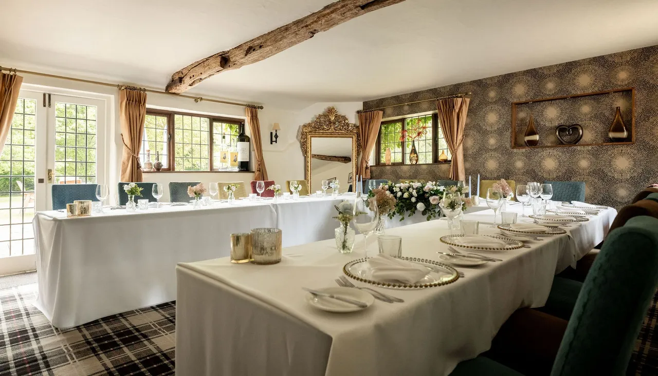 Elegant dining room setup with white tablecloths, floral centerpieces, and decorative elements in a cozy, light-filled space.