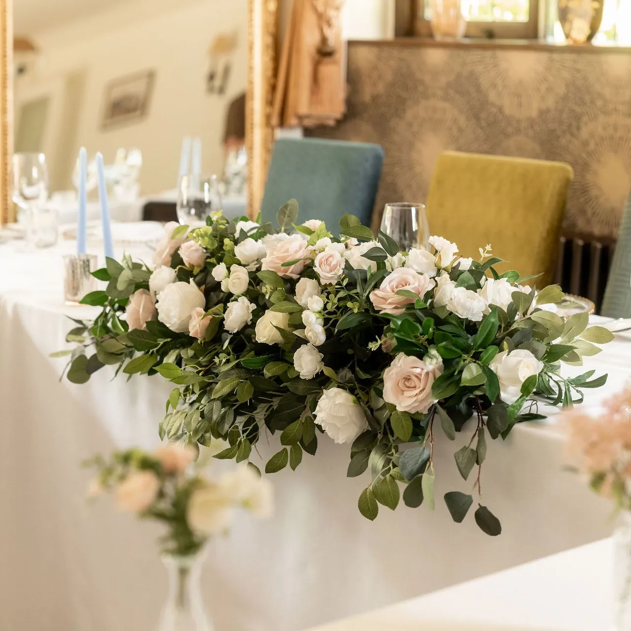Elegant wedding table arrangement with white and blush pink flowers, greenery, and light blue candles.