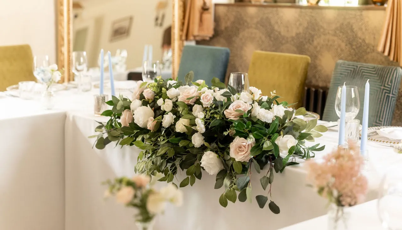 Elegant wedding table arrangement with white and blush pink flowers, greenery, and light blue candles.