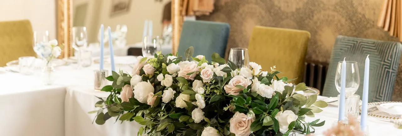 Elegant wedding table arrangement with white and blush pink flowers, greenery, and light blue candles.