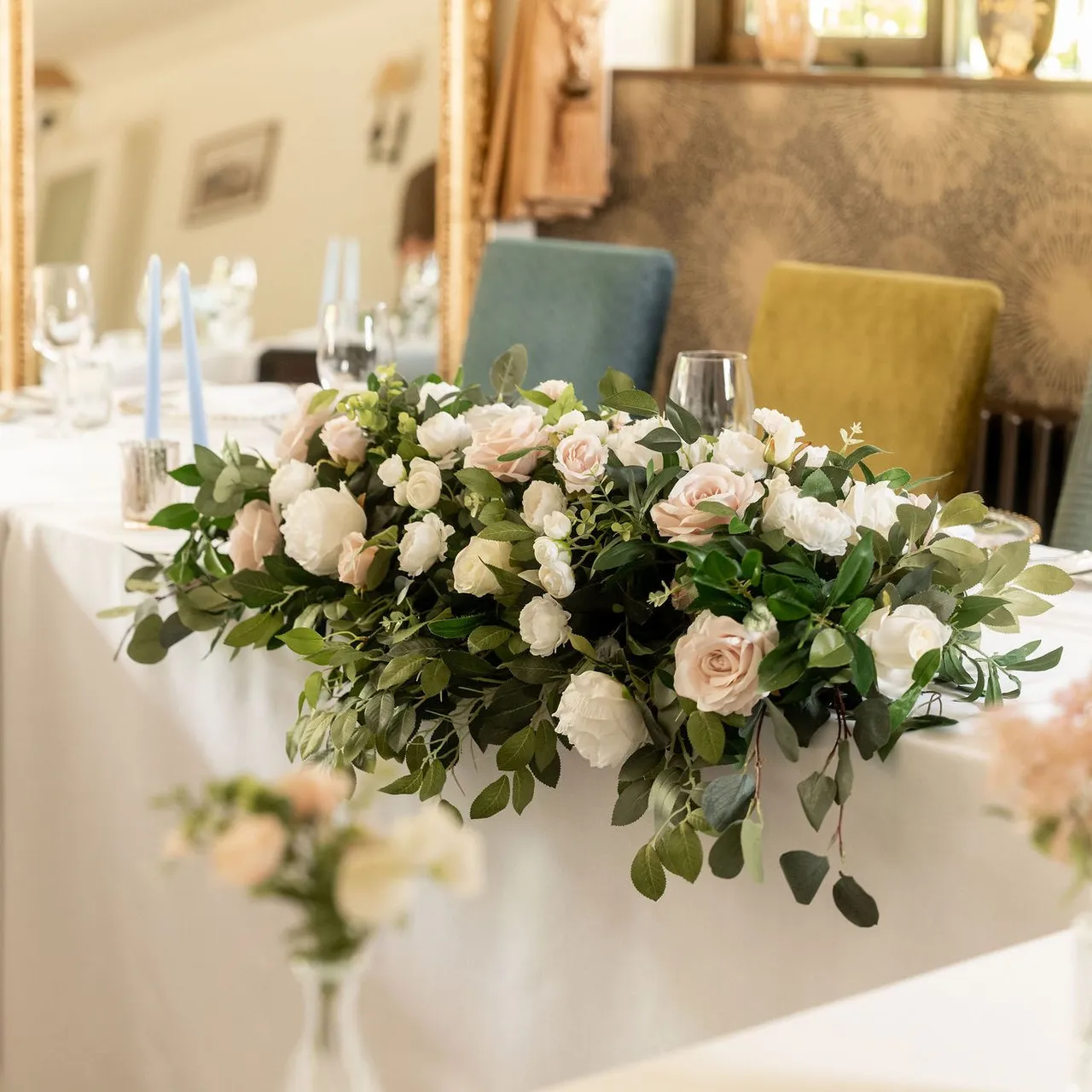 Elegant wedding table arrangement with white and blush pink flowers, greenery, and light blue candles.