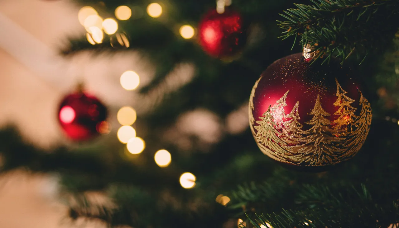 Close-up of a red Christmas ornament with gold tree designs hanging on a Christmas tree