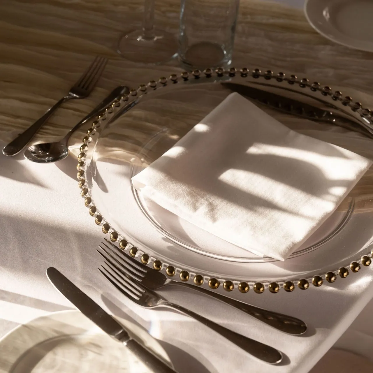 Elegant table setting with glass plate, white napkin, glasses, and silverware in sunlight