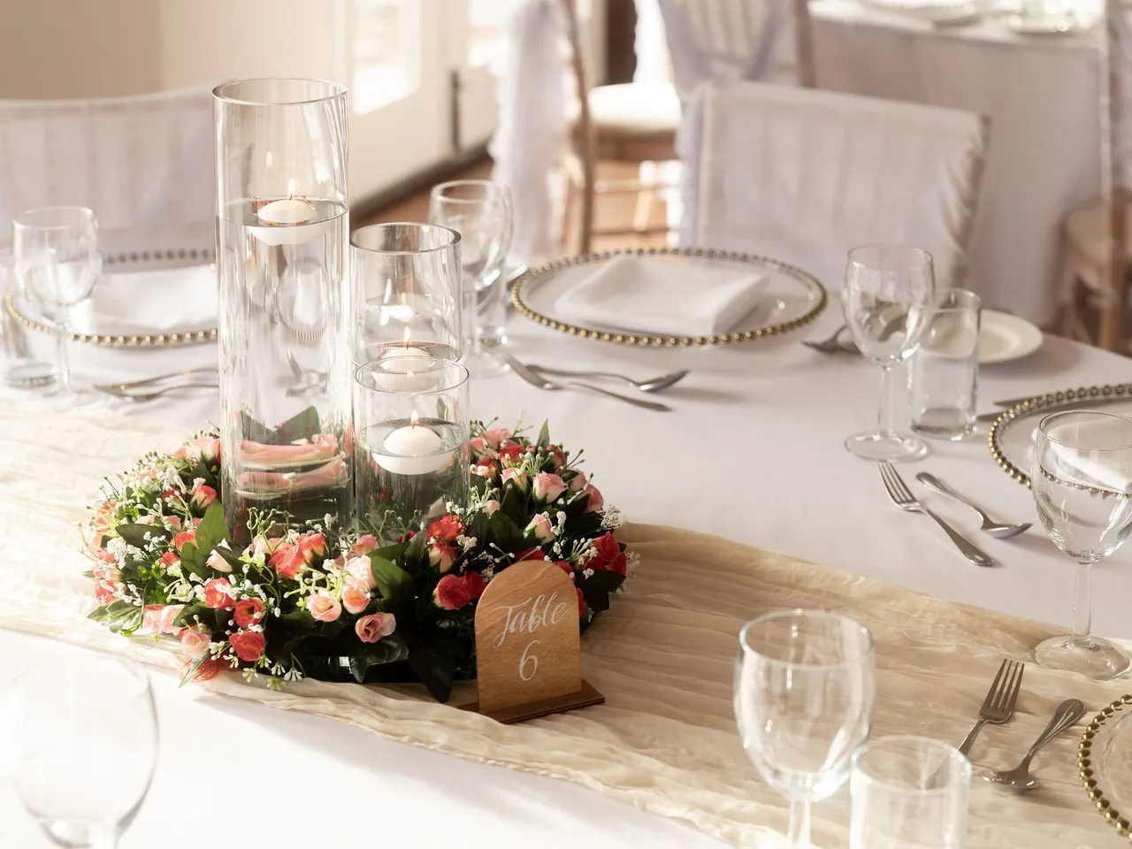 Elegant wedding table setting with glass candle holders, floral centerpiece, and table number 6.
