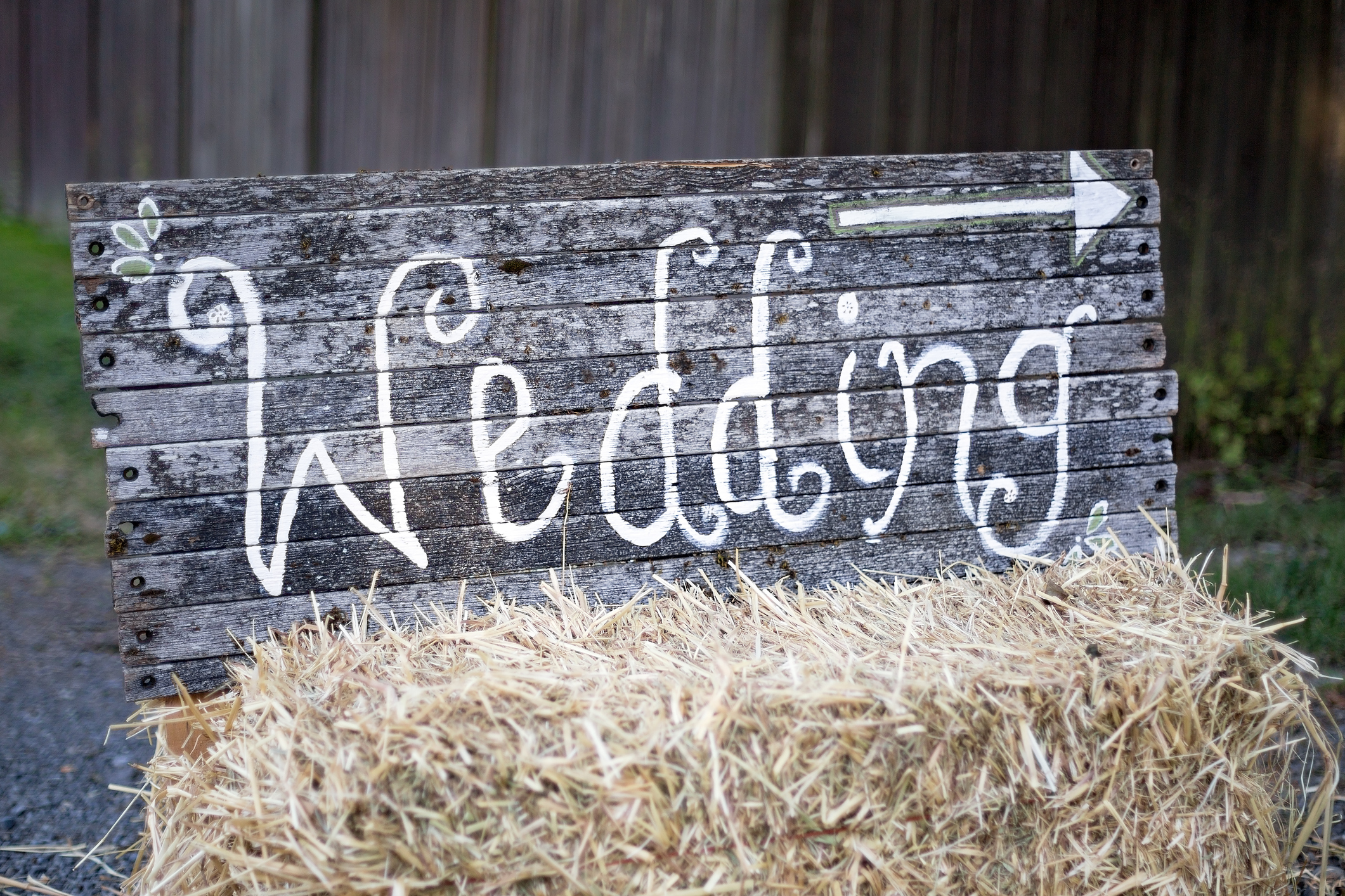 Rustic wooden sign reading “Wedding” with a right-pointing arrow, propped on a hay bale outdoors.